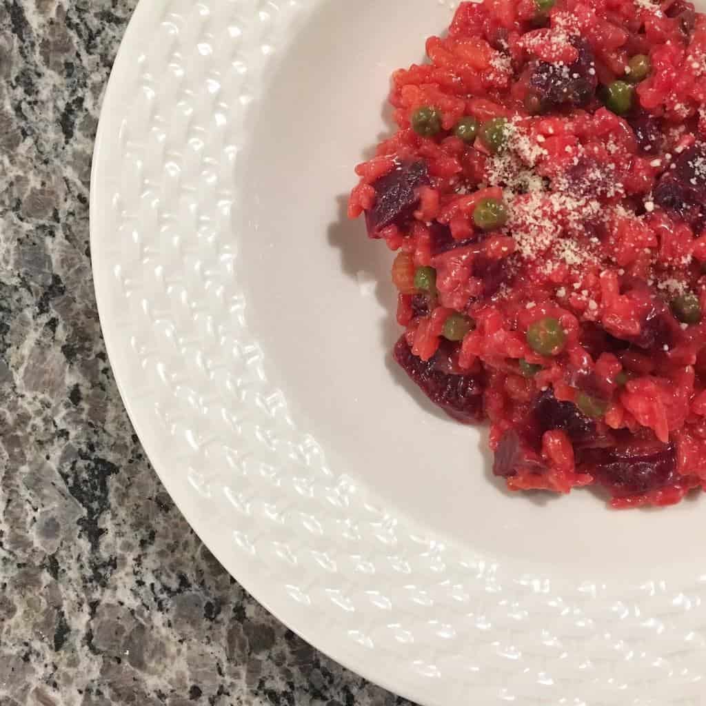 beet risotto with peas in a white bowl, on a grey marble top