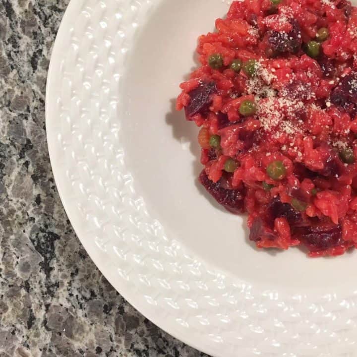 beet risotto with peas in a white bowl, on a grey marble top