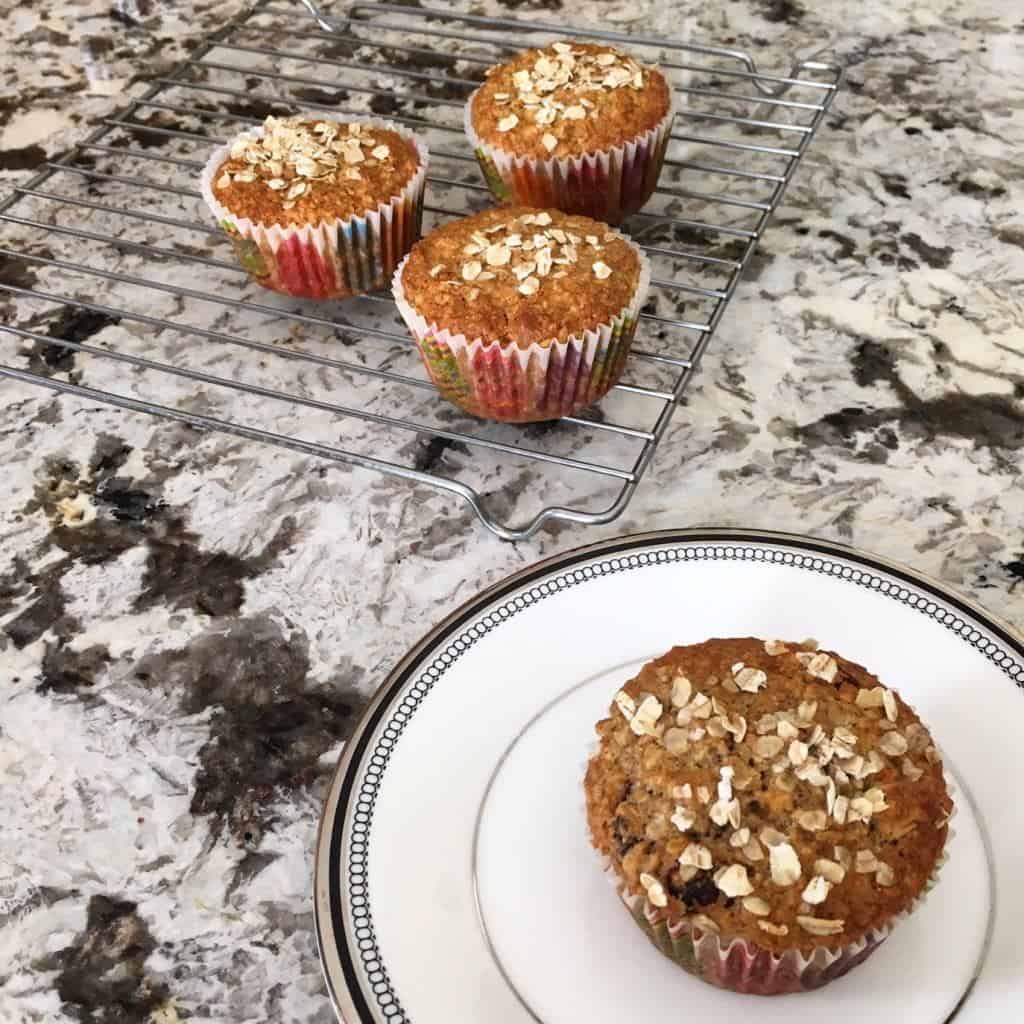 one apple cranberry oatmeal muffin on a plate, 3 more on a cooking rack in the distance