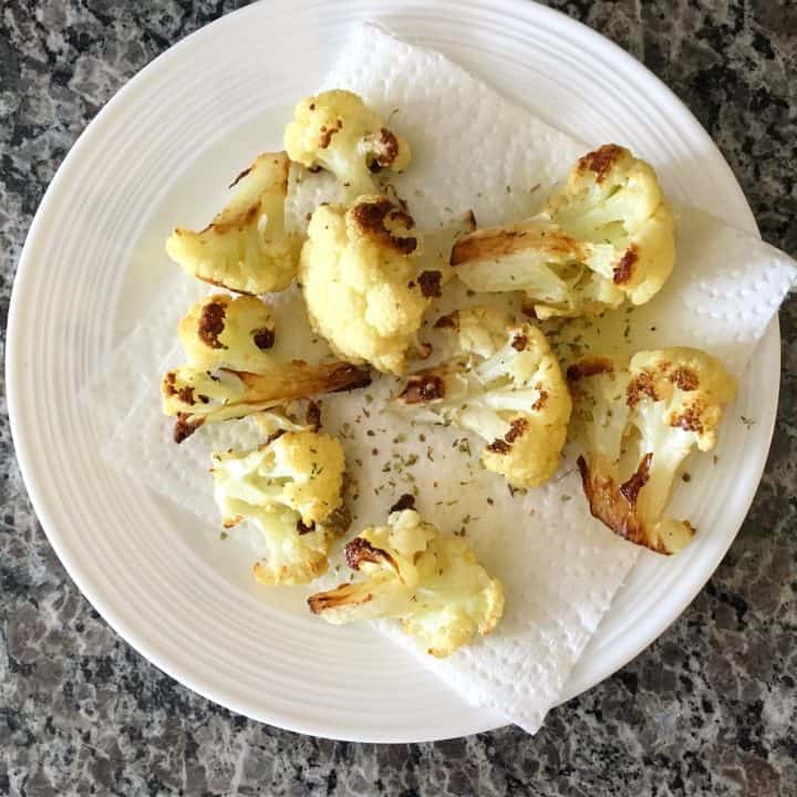 roasted cauliflower on a paper towel, atop a white plate on a grey marble countertop