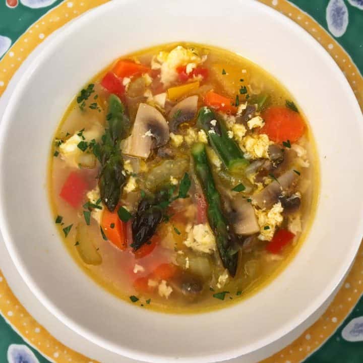 egg drop soup with vegetables in a white bowl