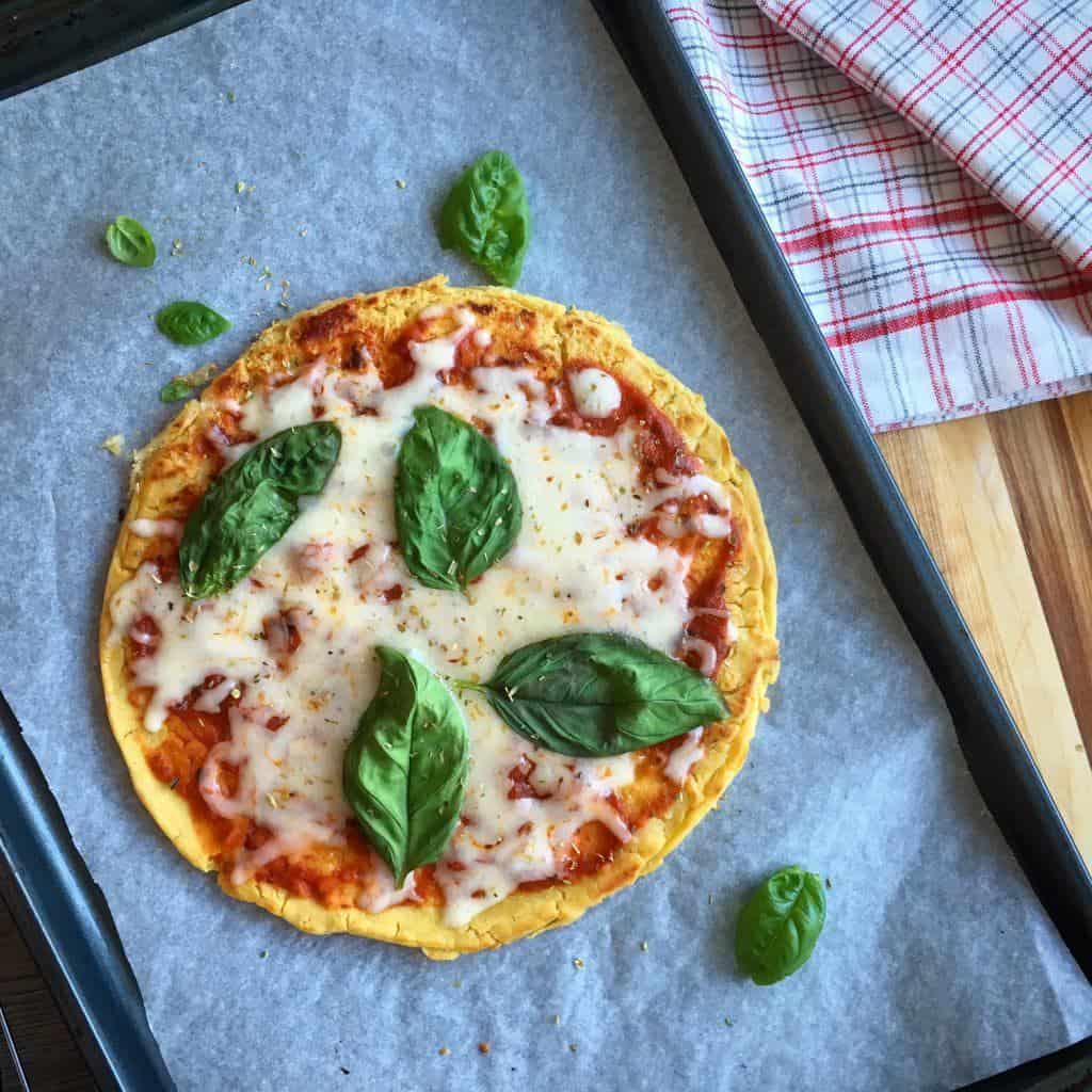 gluten-free pizza with tomato sauce, melted cheese and basil on a parchment lined baking sheet
