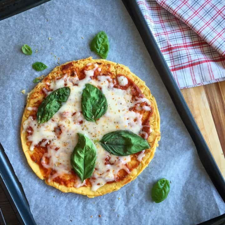 gluten-free pizza with tomato sauce, melted cheese and basil on a parchment lined baking sheet