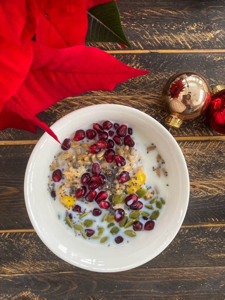 Pomegranate and mango oatmeal with seeds in a white bowl on wooden table.