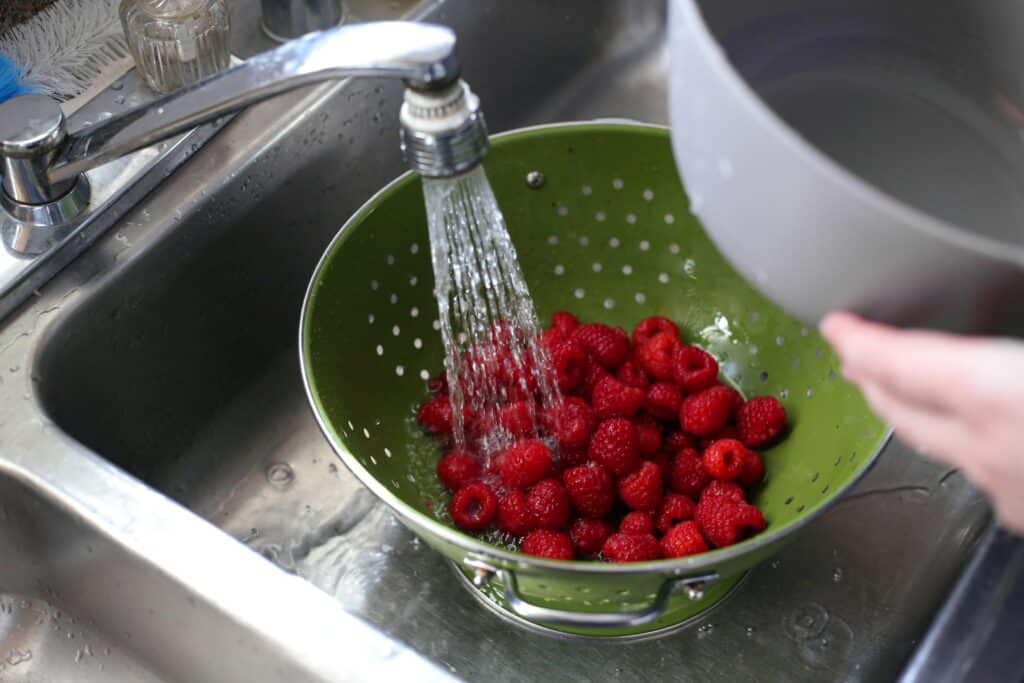 Fresh summer berries washed in a green colander under running water.