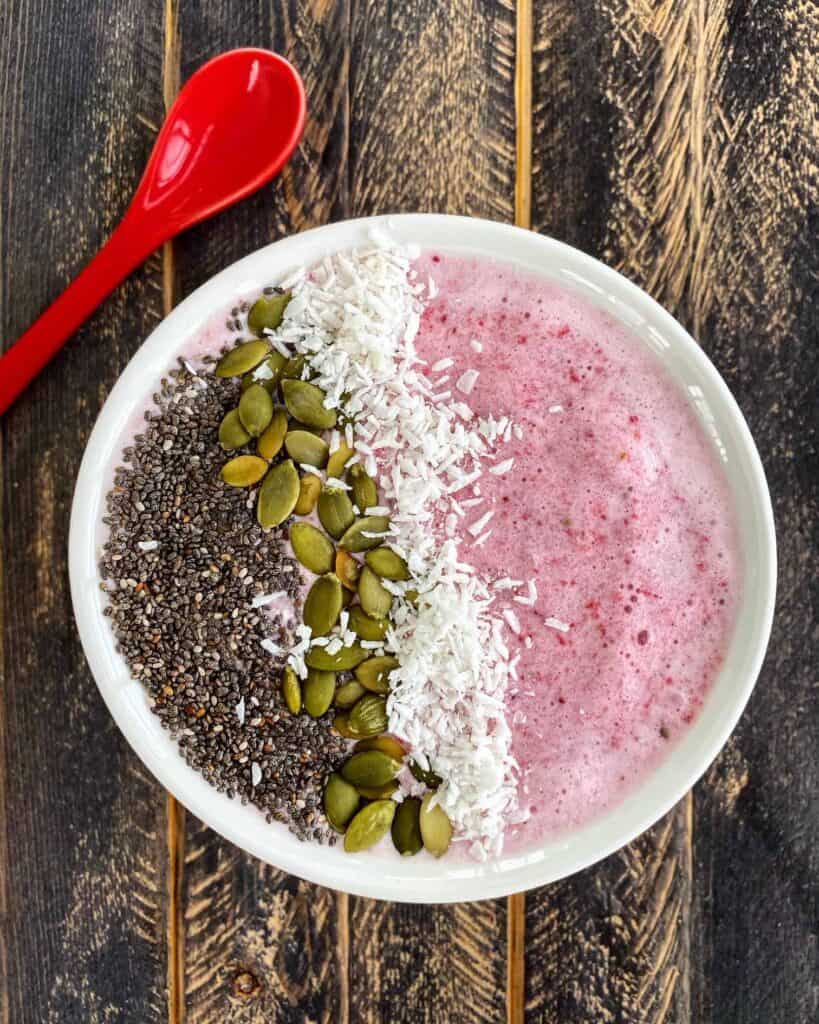 Vibrant smoothie bowl topped with chia seeds, pumpkin seeds, and shredded coconut.