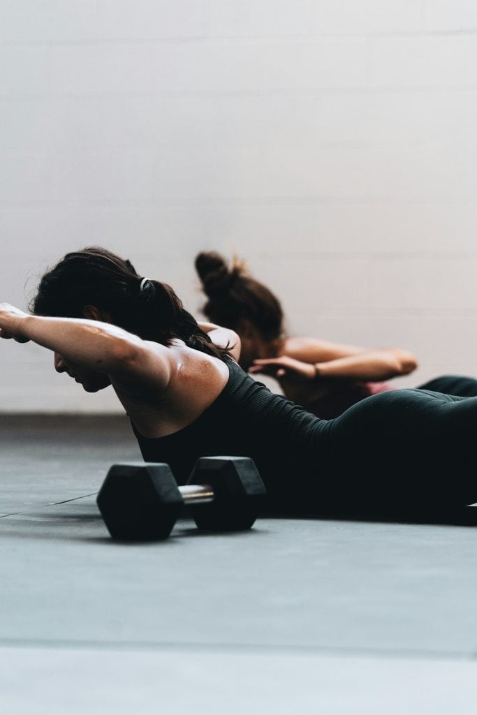 Two women doing core exercises on the floor with dumbbells, promoting fitness and weight management.
